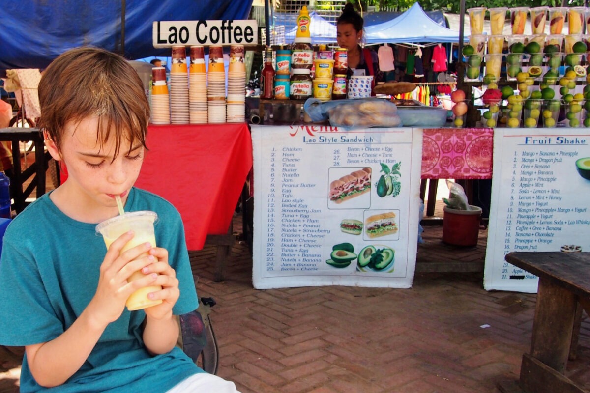 Street food stalls in Laos. Child drinking a smoothie.