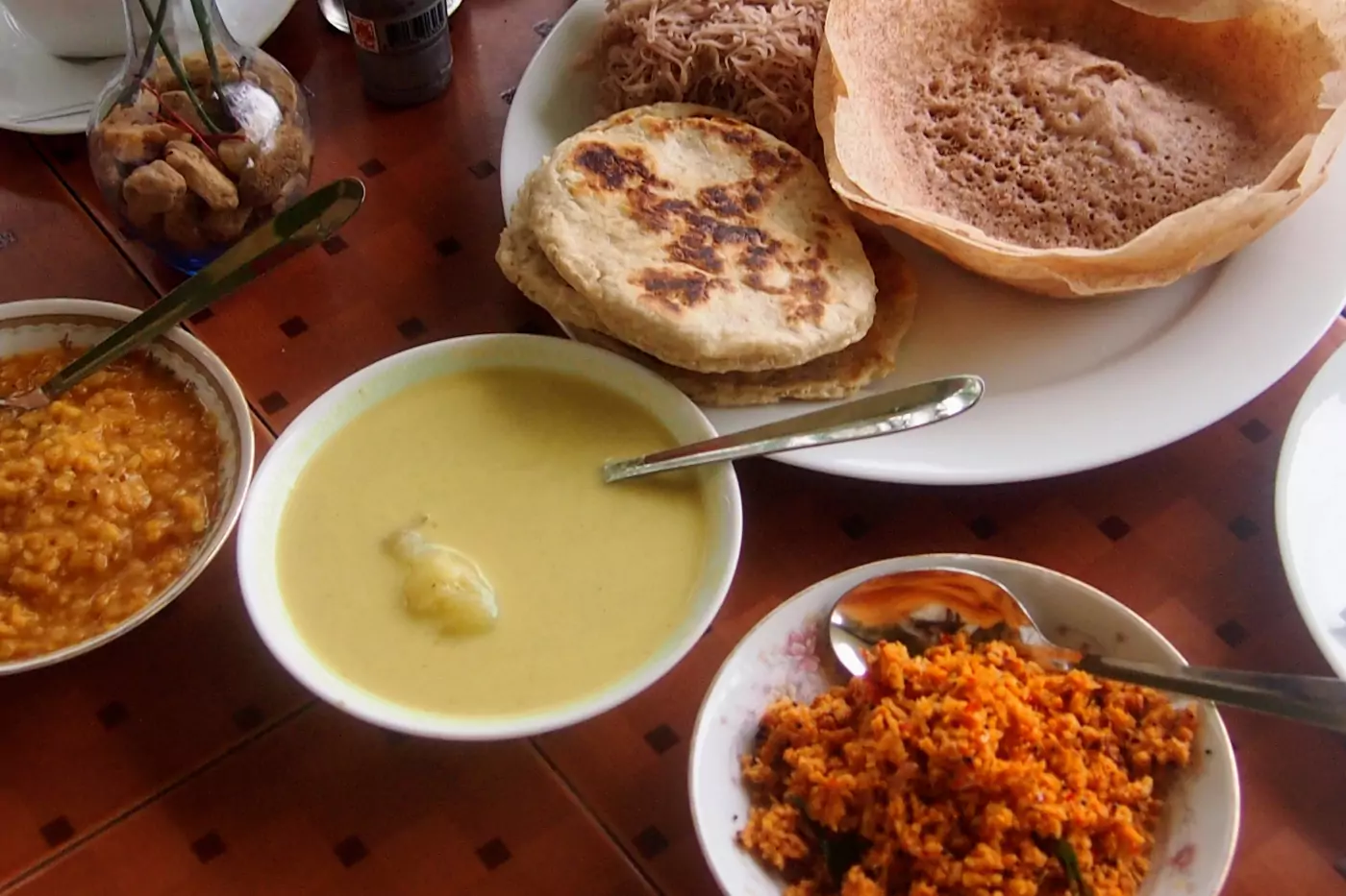 Sri Lankan breakfast foods on a table. Curry, hoppers, roti and coconut chutney.