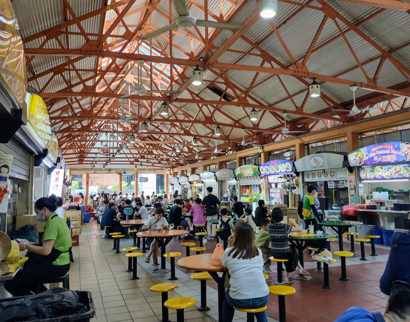 People sitting at tables surrounded by hawker food stalls in a Singapore Chinatown Food court