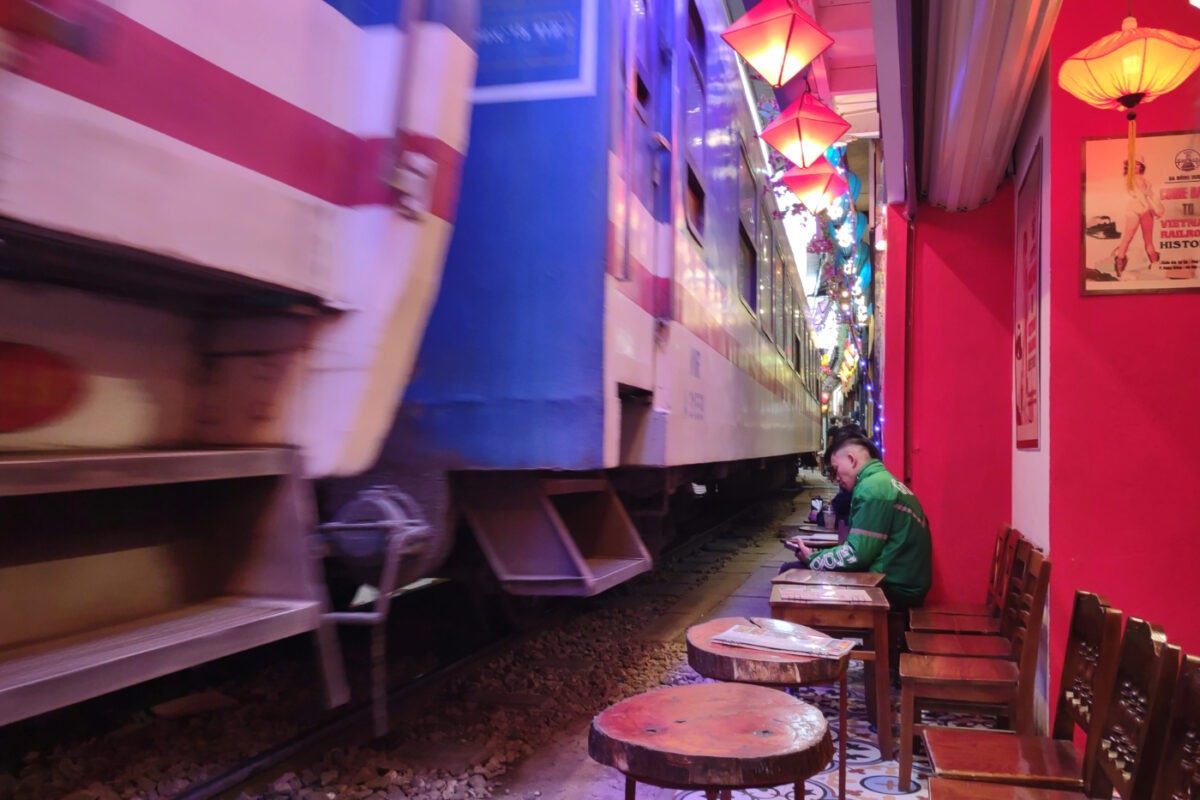 Train passing through a narrow street lined with coffee shops in Hanoi