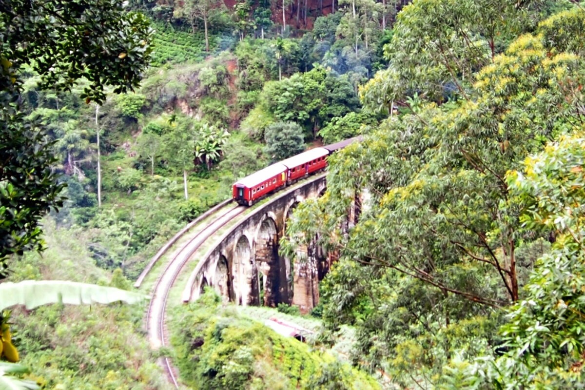 A steam train crossing the railway viaduct outside Ella Sri Lanka. Tea plantations and jungle foliage are visible.