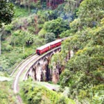 A steam train crossing the railway viaduct outside Ella Sri Lanka. Tea plantations and jungle foliage are visible.