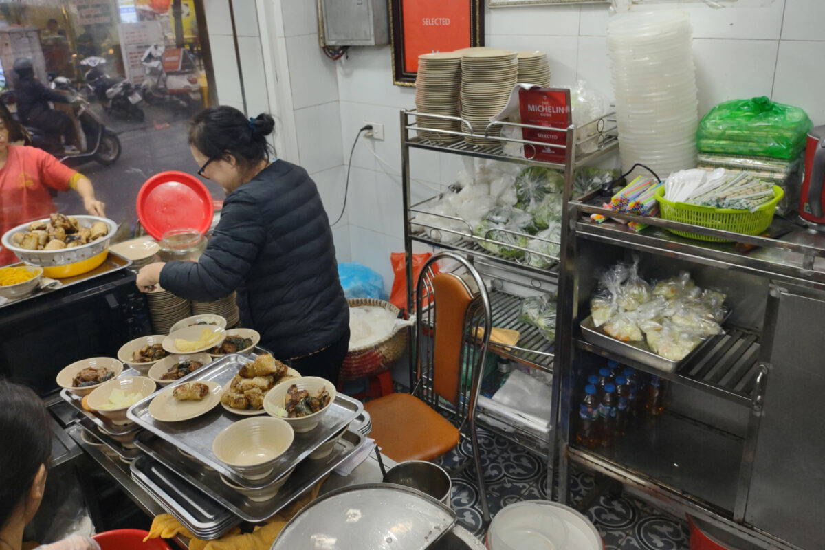 Woman working at a Bun Cha shop in Hanoi. The Michelin Guide certificate is on the wall.